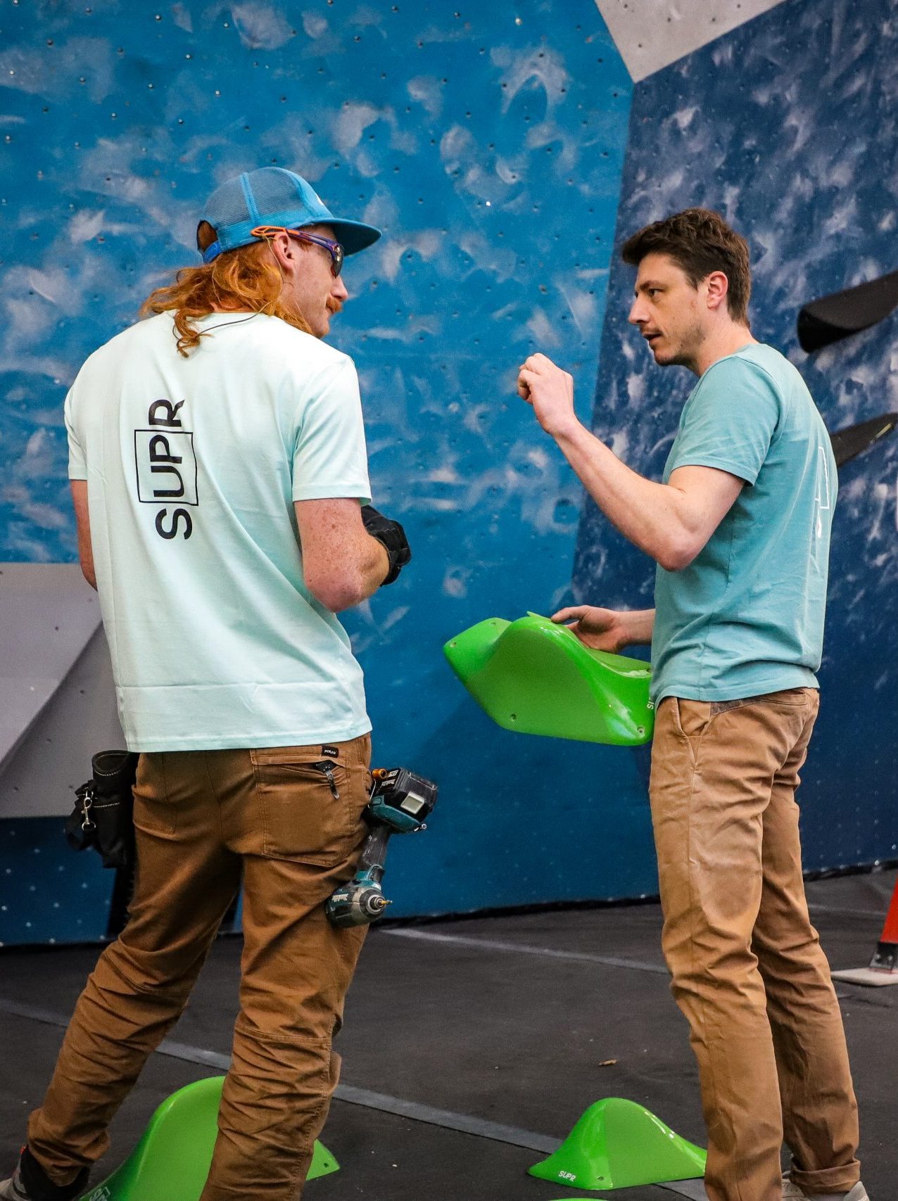 Gautier Supper discussing with someone in a climbing gym. The one on the left has a blue SUP'R t-shirt.